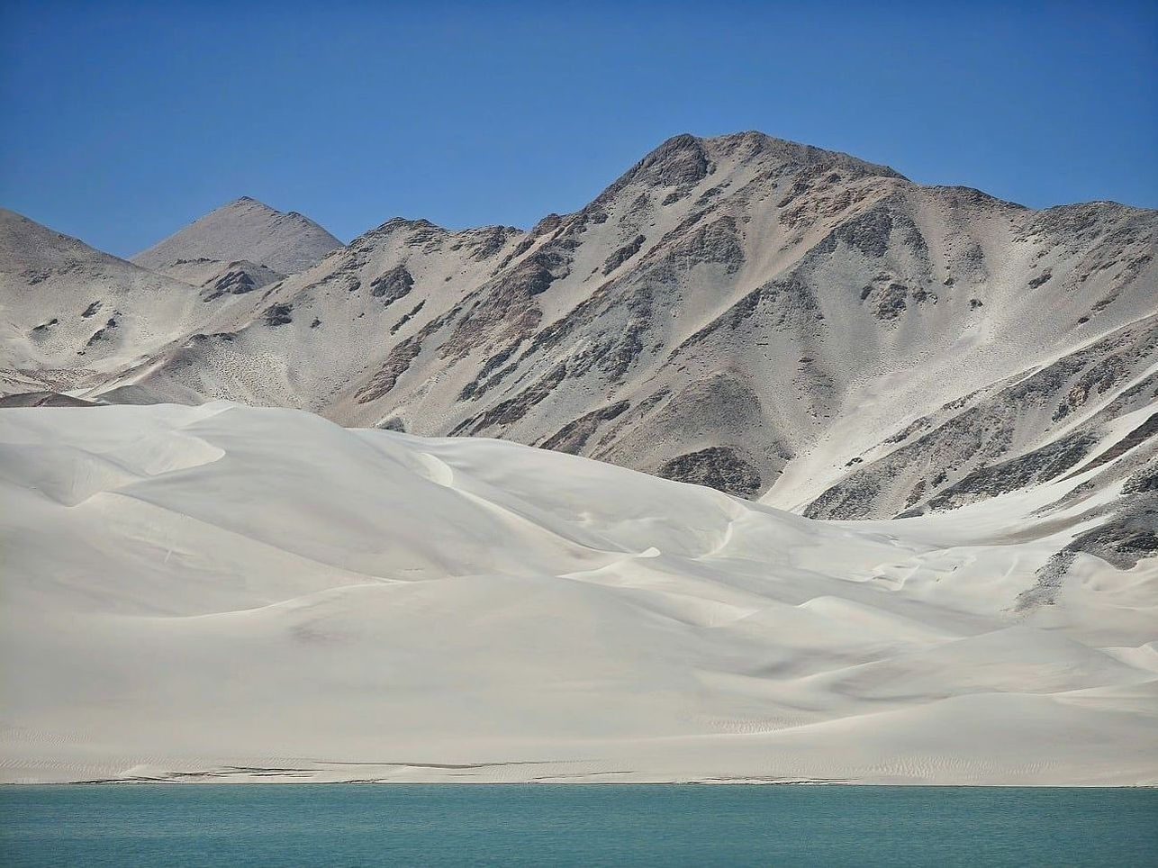 Pescador com vara à beira do lago, montanhas ao fundo coberto de árvores
